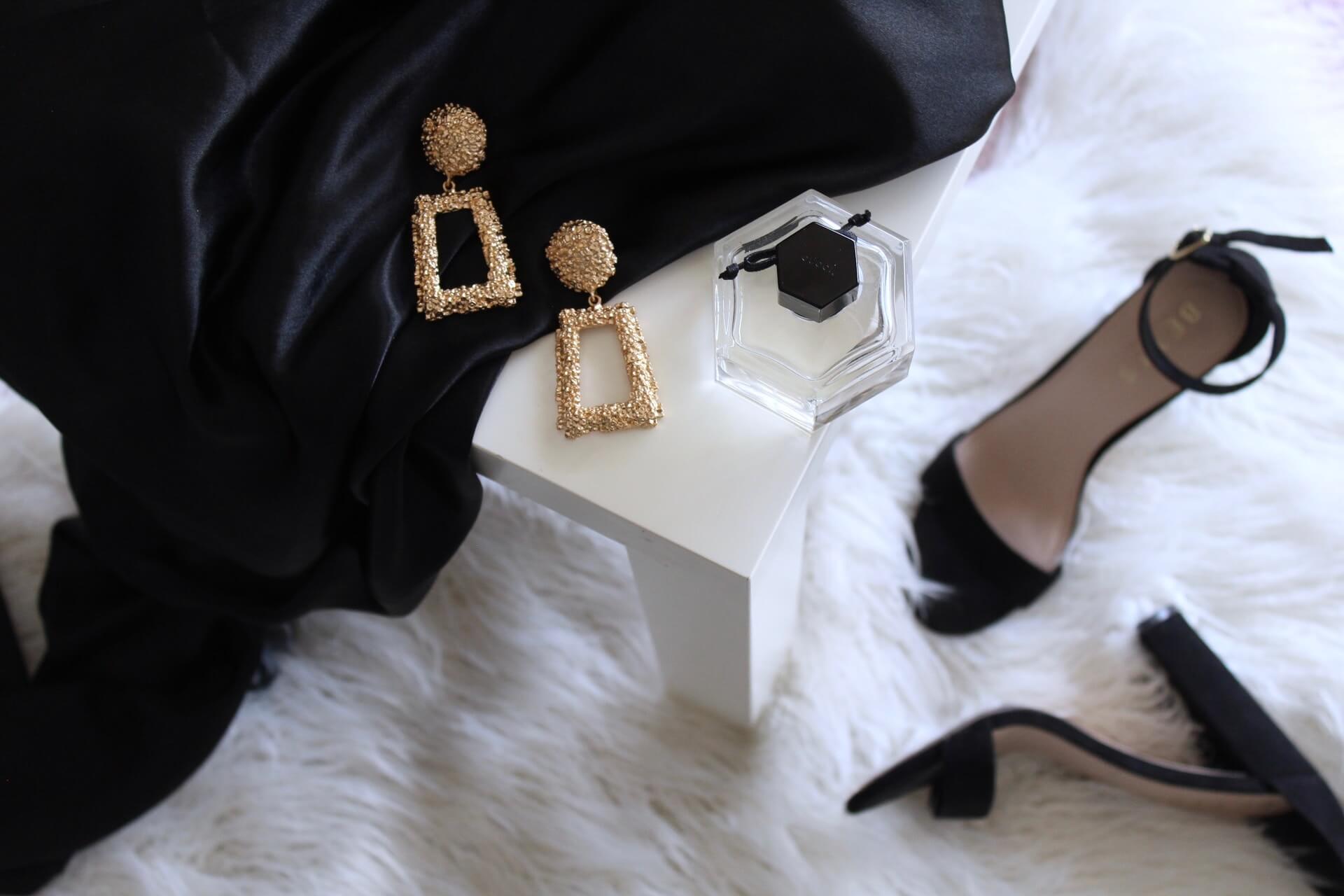 Tee McNeill McNeill Luxury Travel Photo by Gabrielle Henderson pair of gold-colored earrings on table and black ankle-strap pumps on area rug