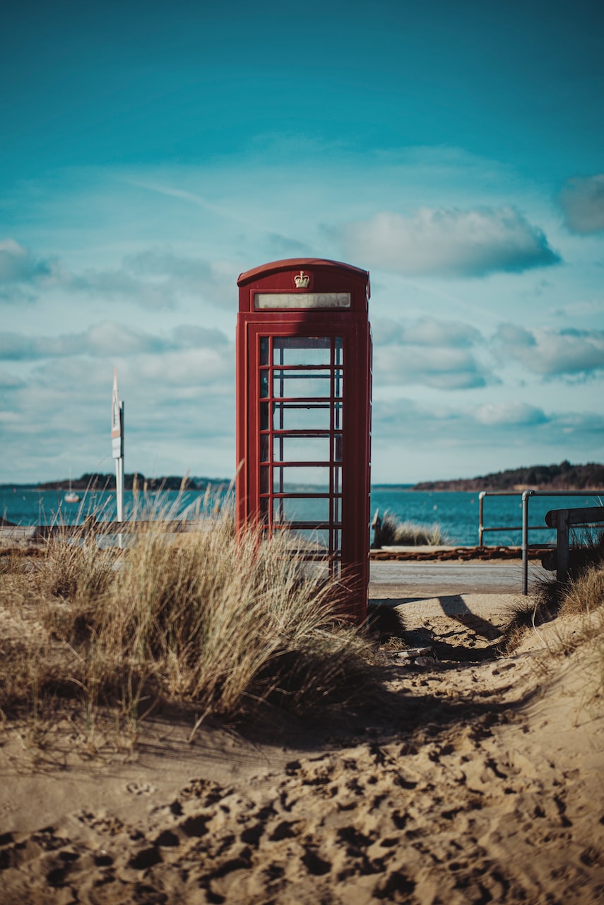 red telephone booth on brown sand under blue sky during daytime